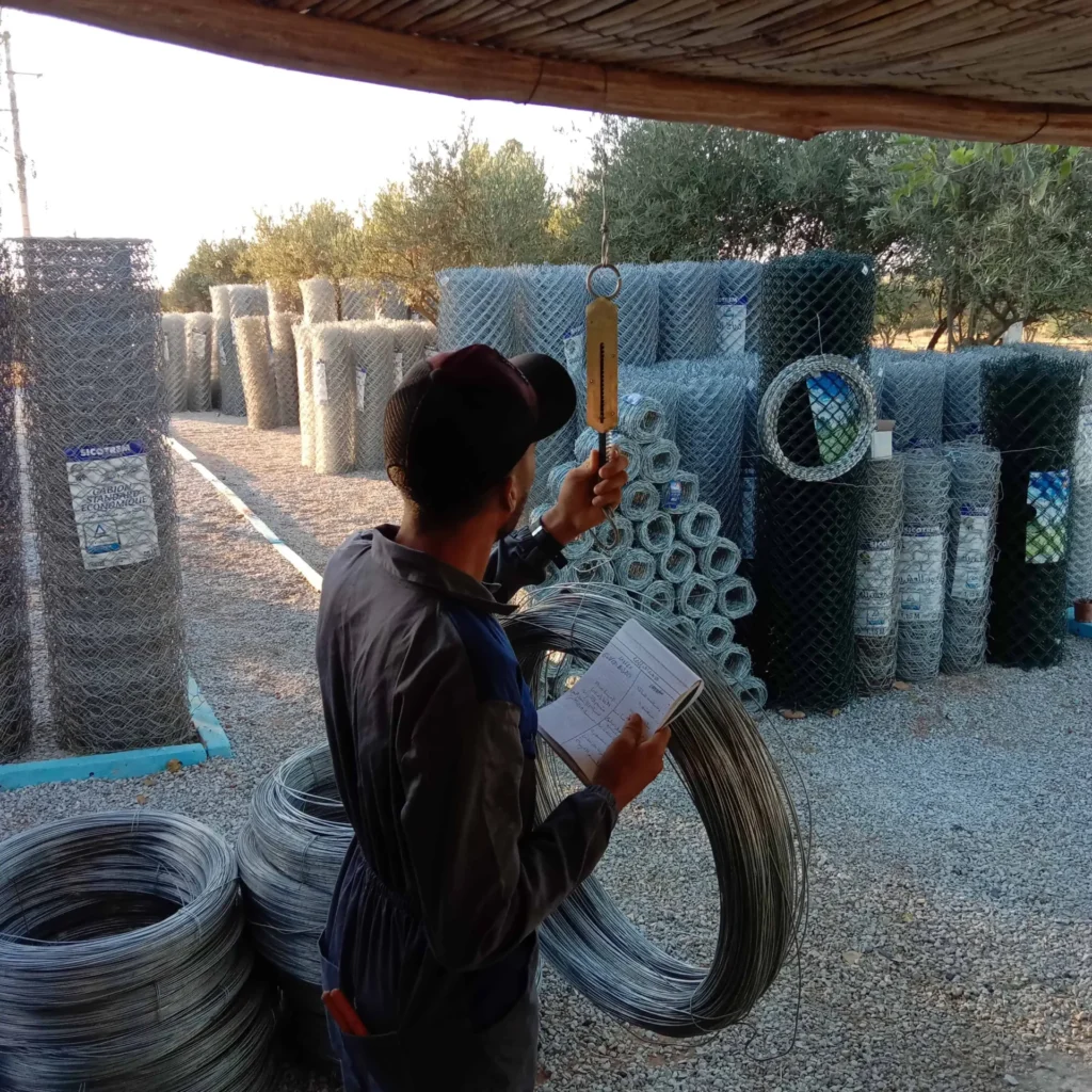 Un travailleur mesurant le poids d'un rouleau de fil de fer lisse pour l'installation d'une clôture agricole.