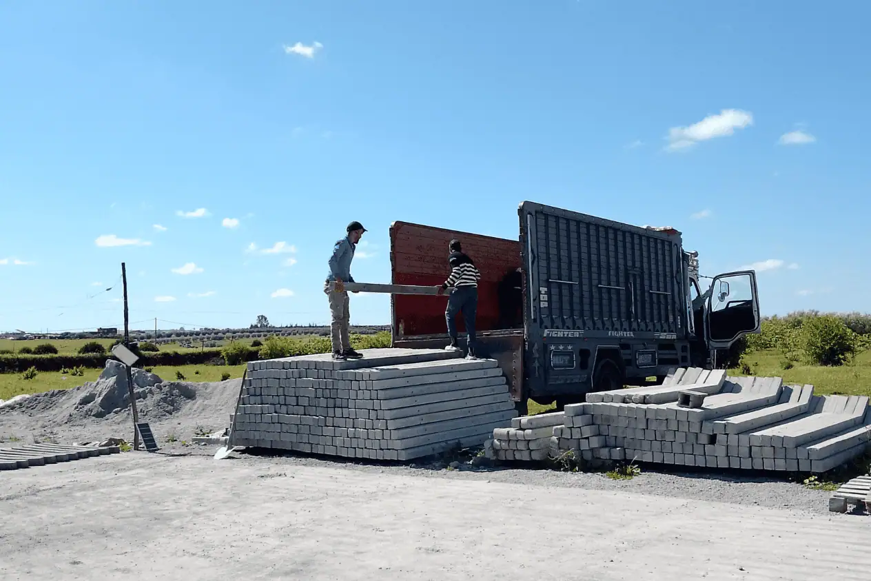 Ouvriers chargeant des poteaux en béton armé sur un camion pour un chantier de clôture au Maroc.