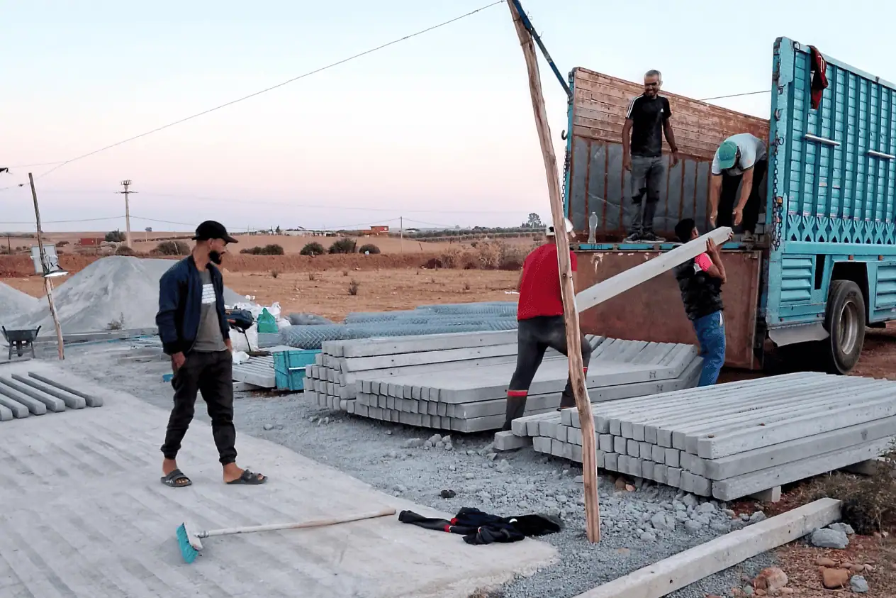 Livraison et déchargement de poteaux en béton armé pour un projet de clôture agricole au Maroc.