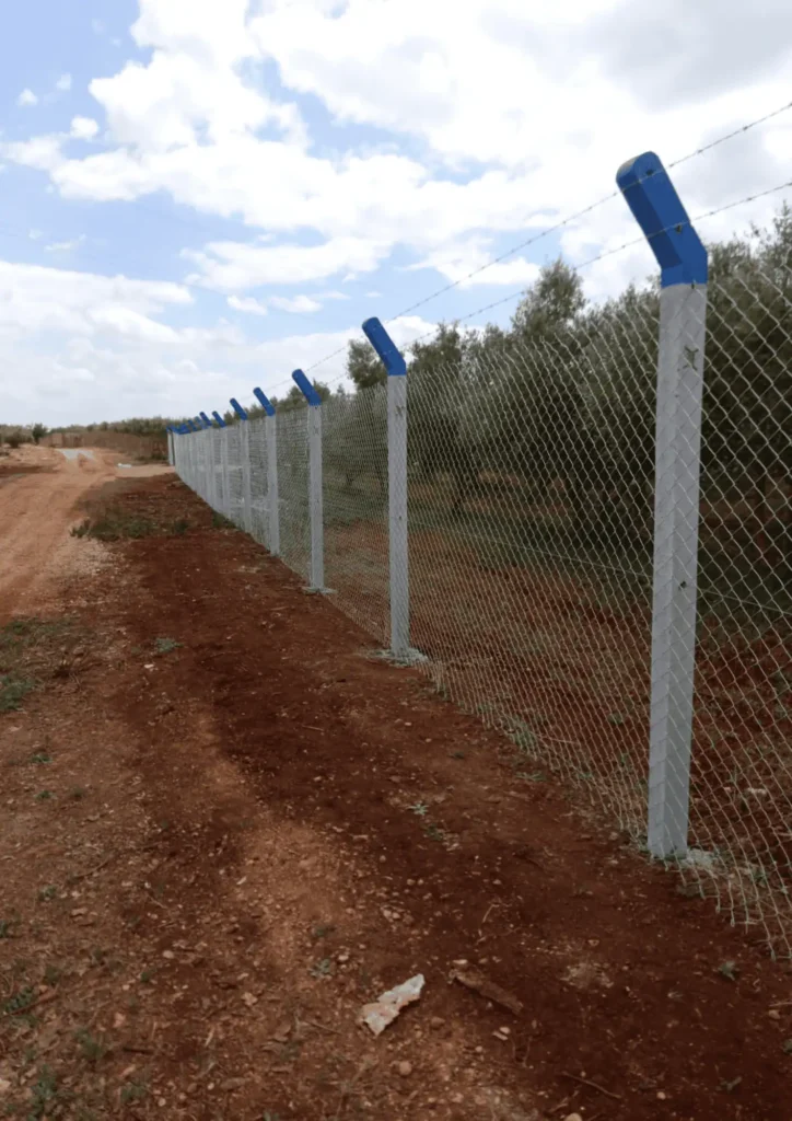 Clôture de sécurité pour terrain agricole avec grillage simple torsion et fils de fer barbelés sur poteaux en béton.